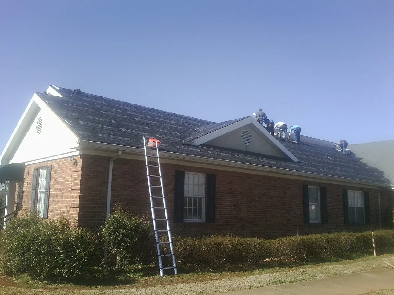 Crew tearing shingles off a brick ranch roof with a ladder set — Metal Roof Repair work by our crew in Saltillo